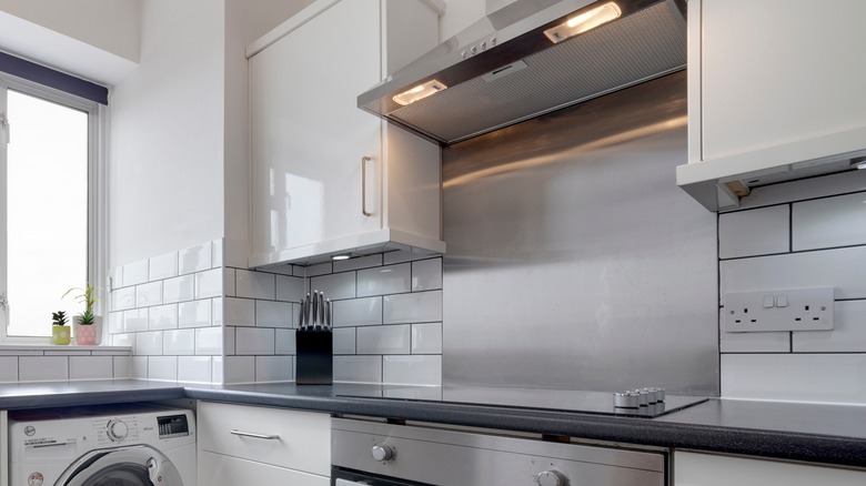 Μια λευκή κουζίνα με ένα ασημένιο backsplash πίσω από το cooktop