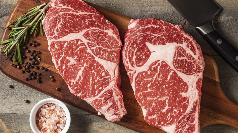 Άψογες μπριζόλες Wagyu σε ένα ξύλινο σκάφος κοπής με πιπεριές, ροζ αλάτι και δεντρολίβανο